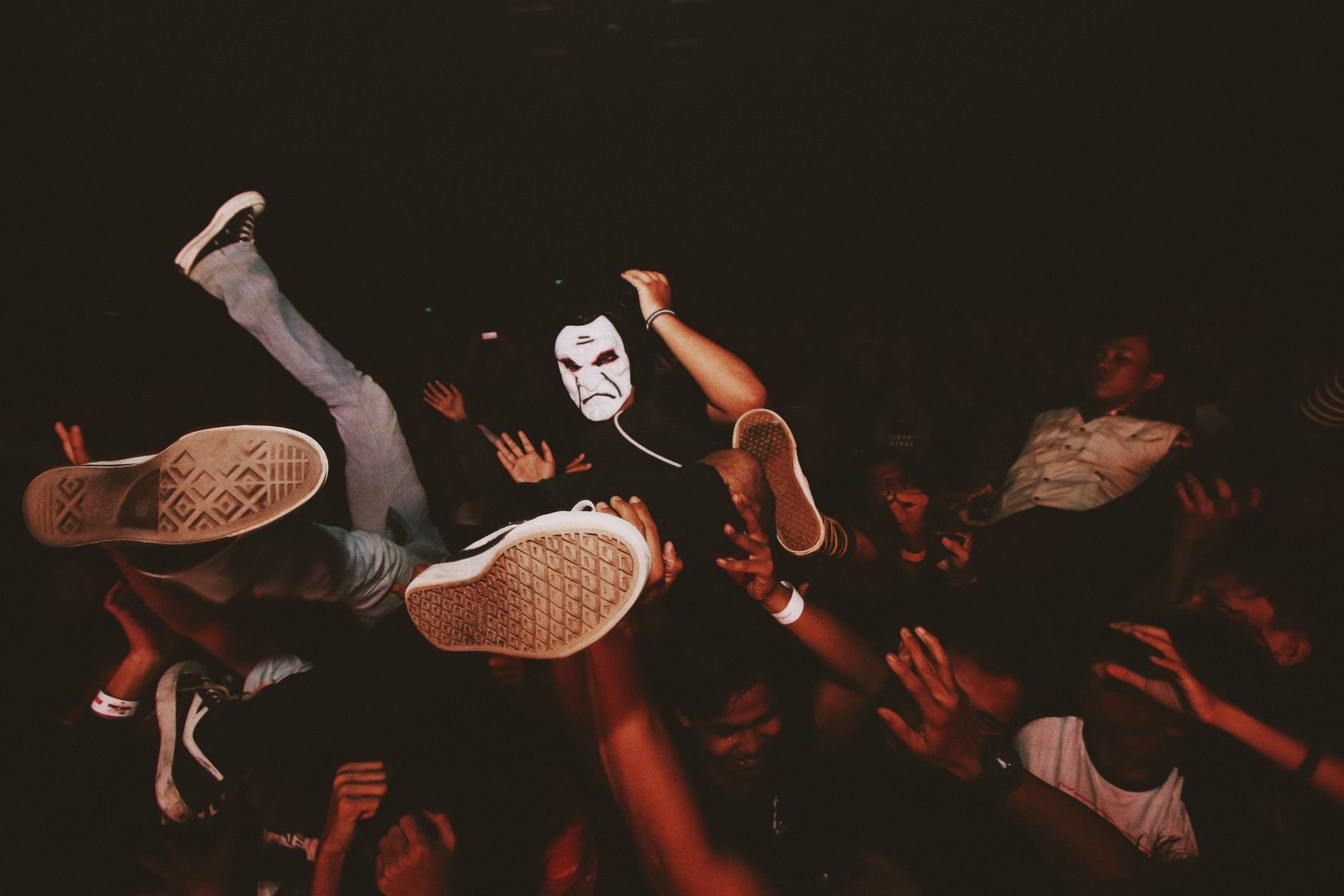 Vibrant crowd at a dark night concert with a masked participant crowd surfing