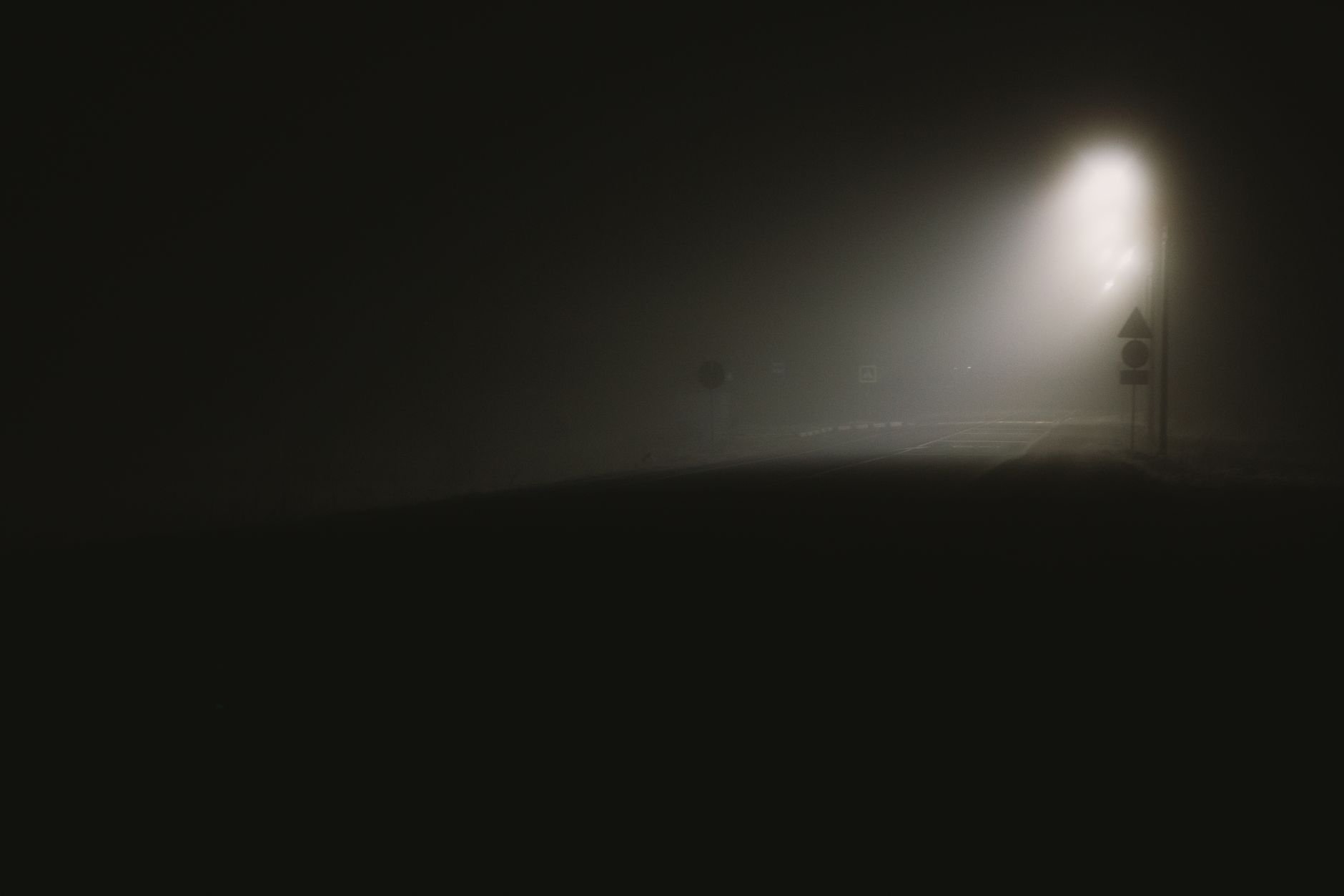 A fog-covered dark street illuminated by a single streetlight at night